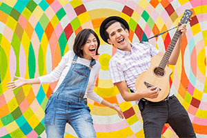 two performers with a guitar in front of a colorful background