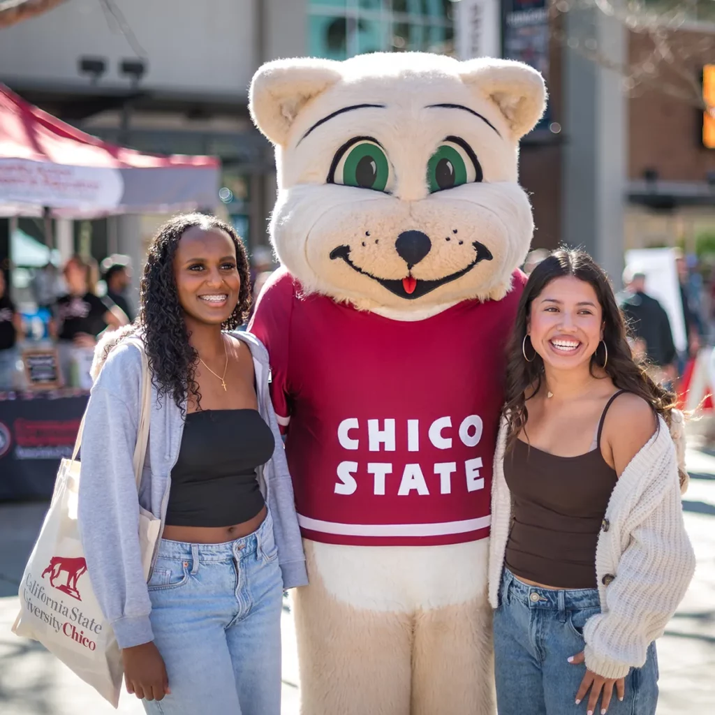Two students smile alongside Willie the Wildcat, Chico State's mascot.