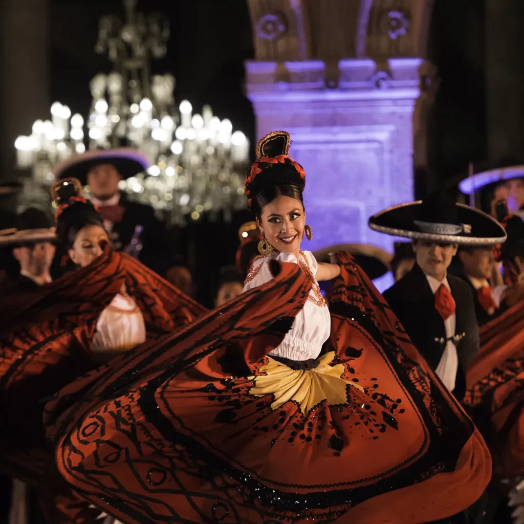 Women dancing in red dresses and men wearing sombreros in Ballet Folklórico de Mexico perfromance.