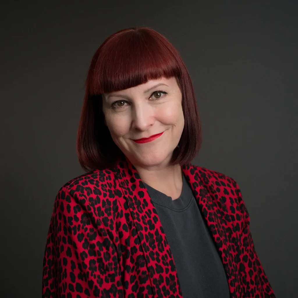 Head shot of Bonnie Pipkin smiling, wearing red lipstick and a red and black leopard print blazer.