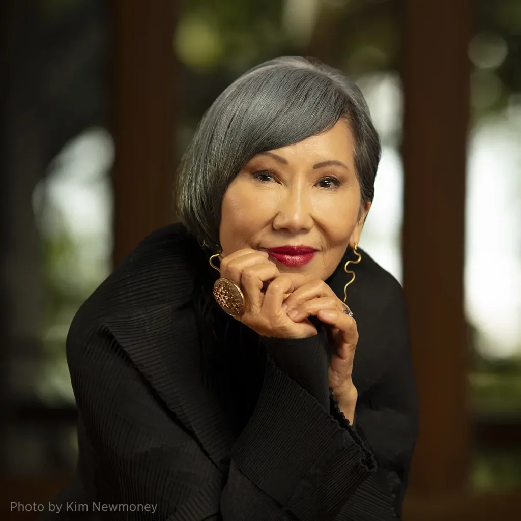 Photo of author Amy Tan, resting her head on her hands and smiling.