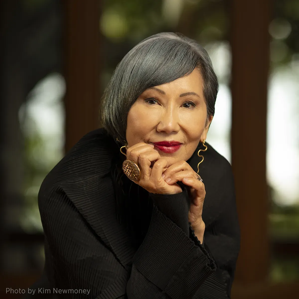 Photo of author Amy Tan, resting her head on her hands and smiling.
