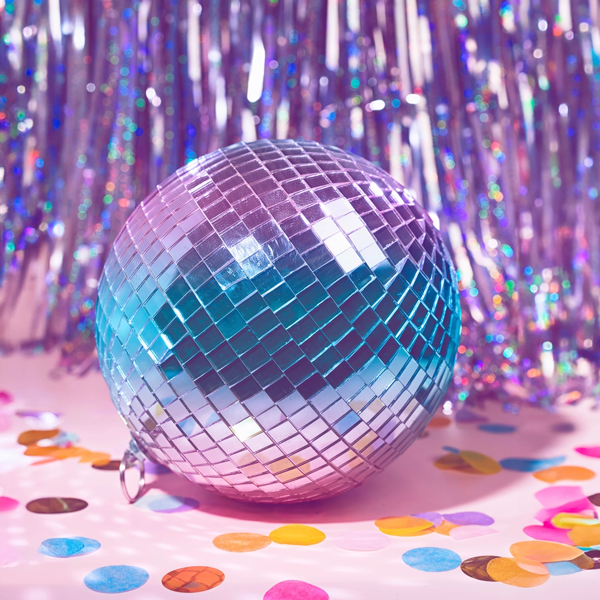 Disco ball with tinsel wall behind and confetti in foreground.